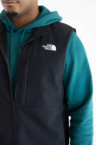 A person wearing a black vest over a teal hoodie, with The North Face logo printed in white on the upper right chest.