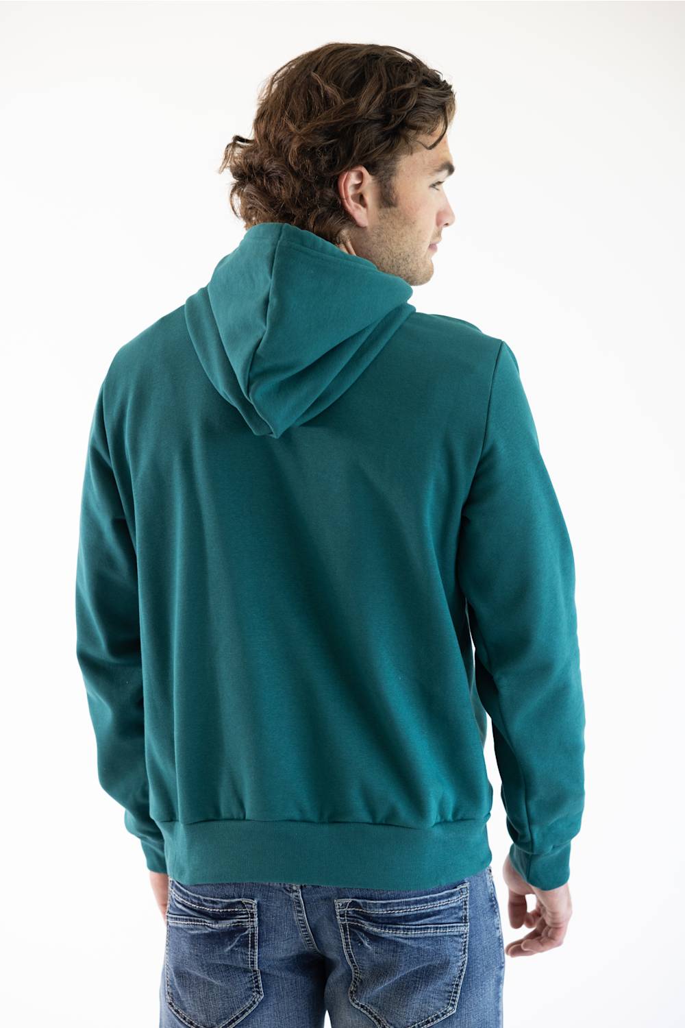 A man viewed from the back wearing a teal green pullover hoodie with a white square The North Face logo patch on the left chest, paired with blue jeans, photographed against a plain white studio background.