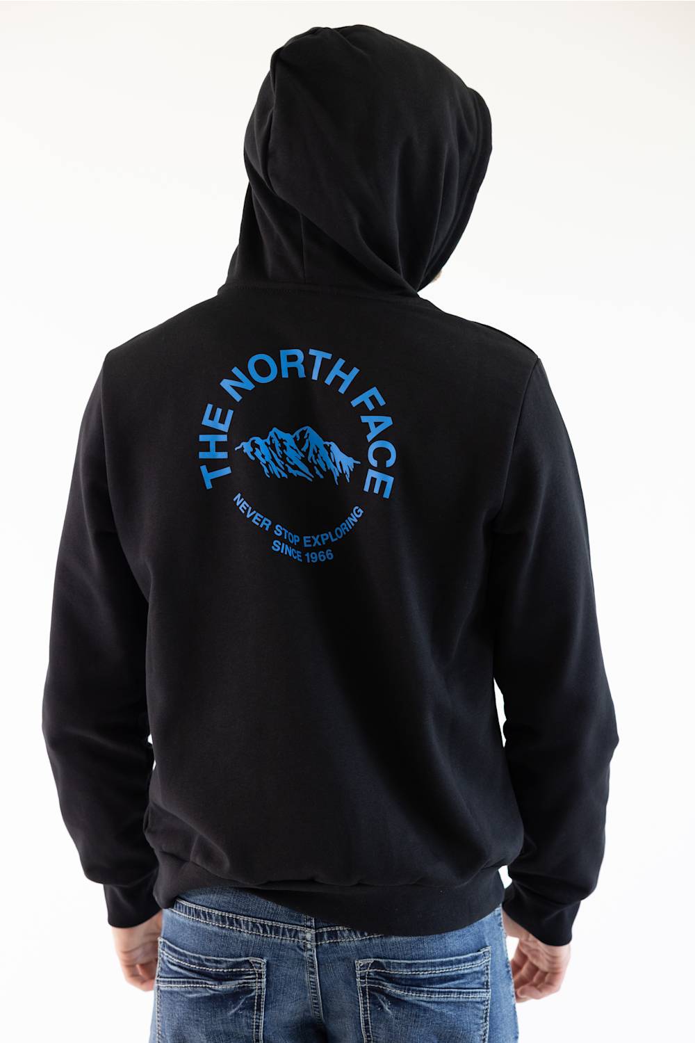 A man viewed from the back wearing a black hoodie featuring a blue graphic print of a mountain range with the text 'THE NORTH FACE' and 'NEVER STOP EXPLORING SINCE 1966'.
