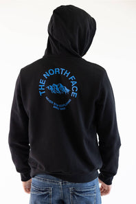 A man viewed from the back wearing a black hoodie featuring a blue graphic print of a mountain range with the text 'THE NORTH FACE' and 'NEVER STOP EXPLORING SINCE 1966'.