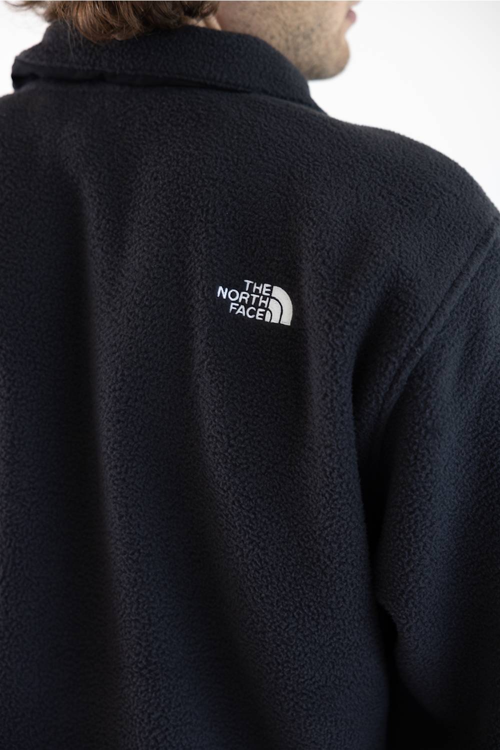 Close-up back view of a person wearing a dark navy fleece jacket with a white embroidered The North Face logo on the upper back.