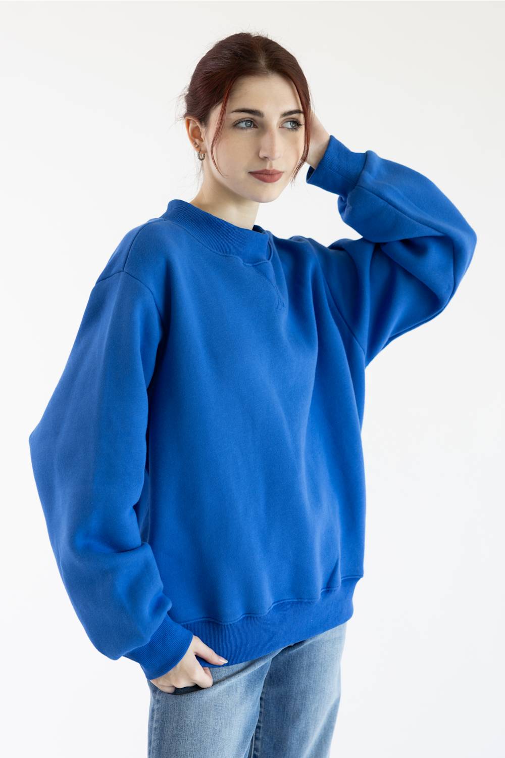 A woman wearing an oversized royal blue sweatshirt and light blue jeans, posing against a plain white studio background.