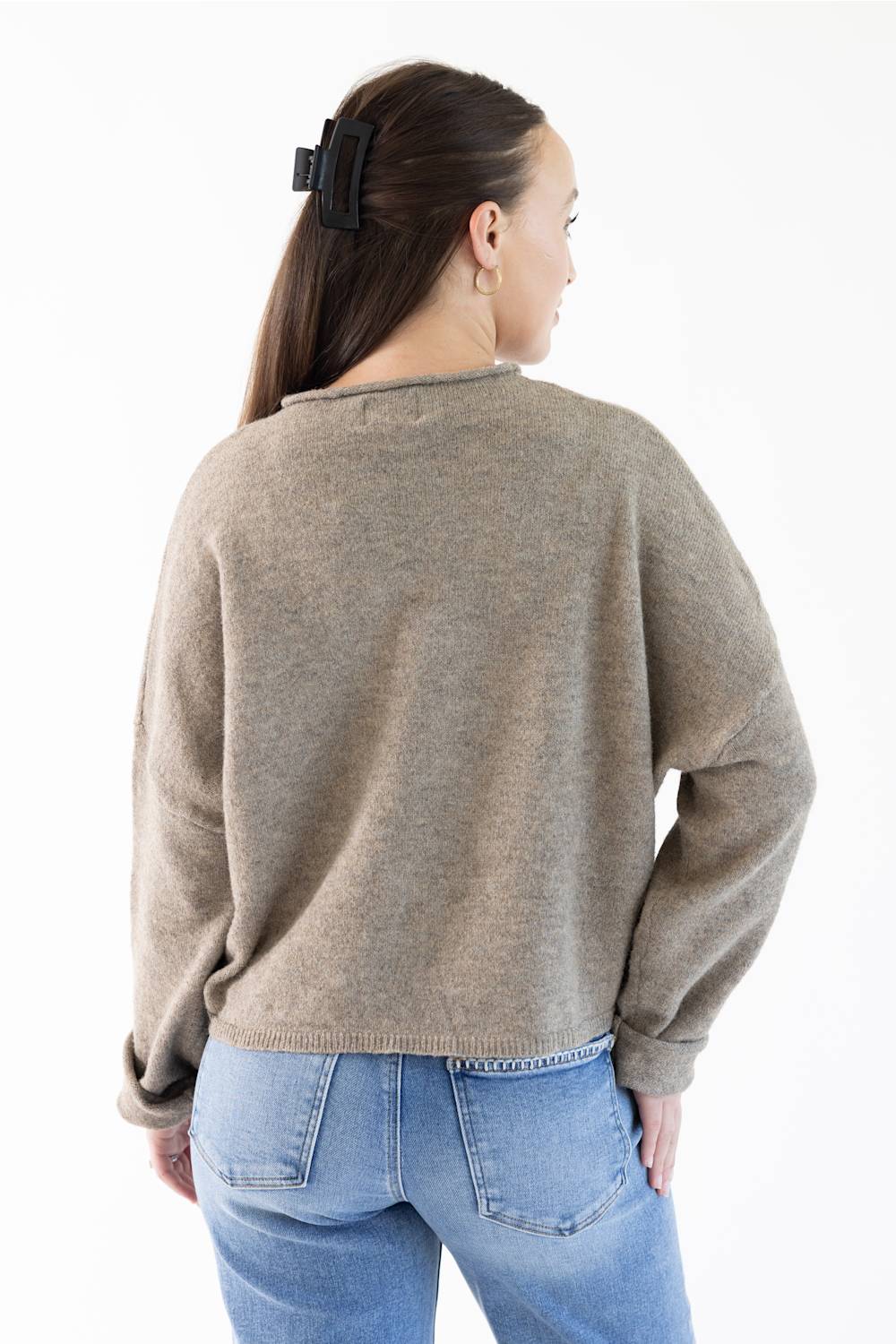 A woman shown from the back wearing a light brown knit sweater and blue jeans against a plain white background.