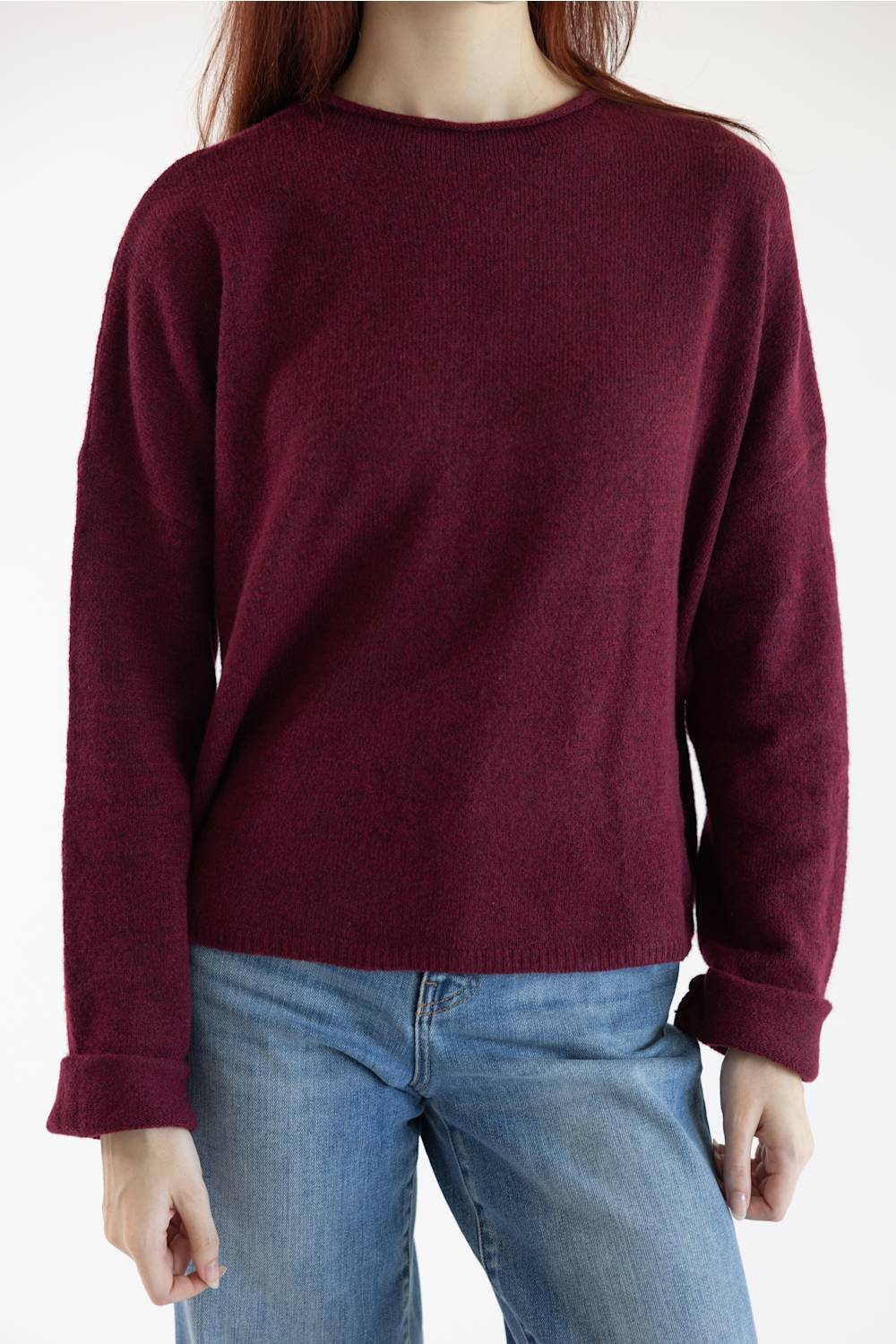 A person wearing a crewneck knit sweater in deep burgundy with light blue jeans, shown from the neck down against a plain white background.