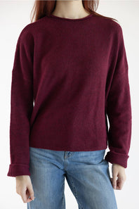 A person wearing a crewneck knit sweater in deep burgundy with light blue jeans, shown from the neck down against a plain white background.