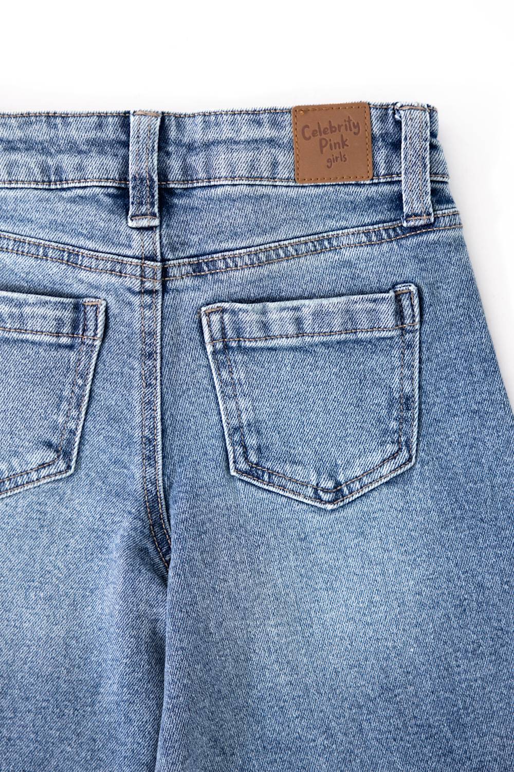 Close-up back view of light blue denim jeans showing the waistband, belt loops, and back pockets. A brown leather patch near the waistband reads 'Celebrity Pink 2018'.