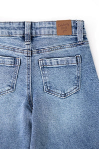 Close-up back view of light blue denim jeans showing the waistband, belt loops, and back pockets. A brown leather patch near the waistband reads 'Celebrity Pink 2018'.