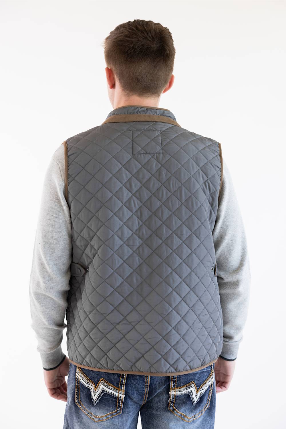A male model shown from the back wearing the charcoal FX Fusion Upland Quilted Field Vest with brown trim, over a grey sweater and blue jeans.