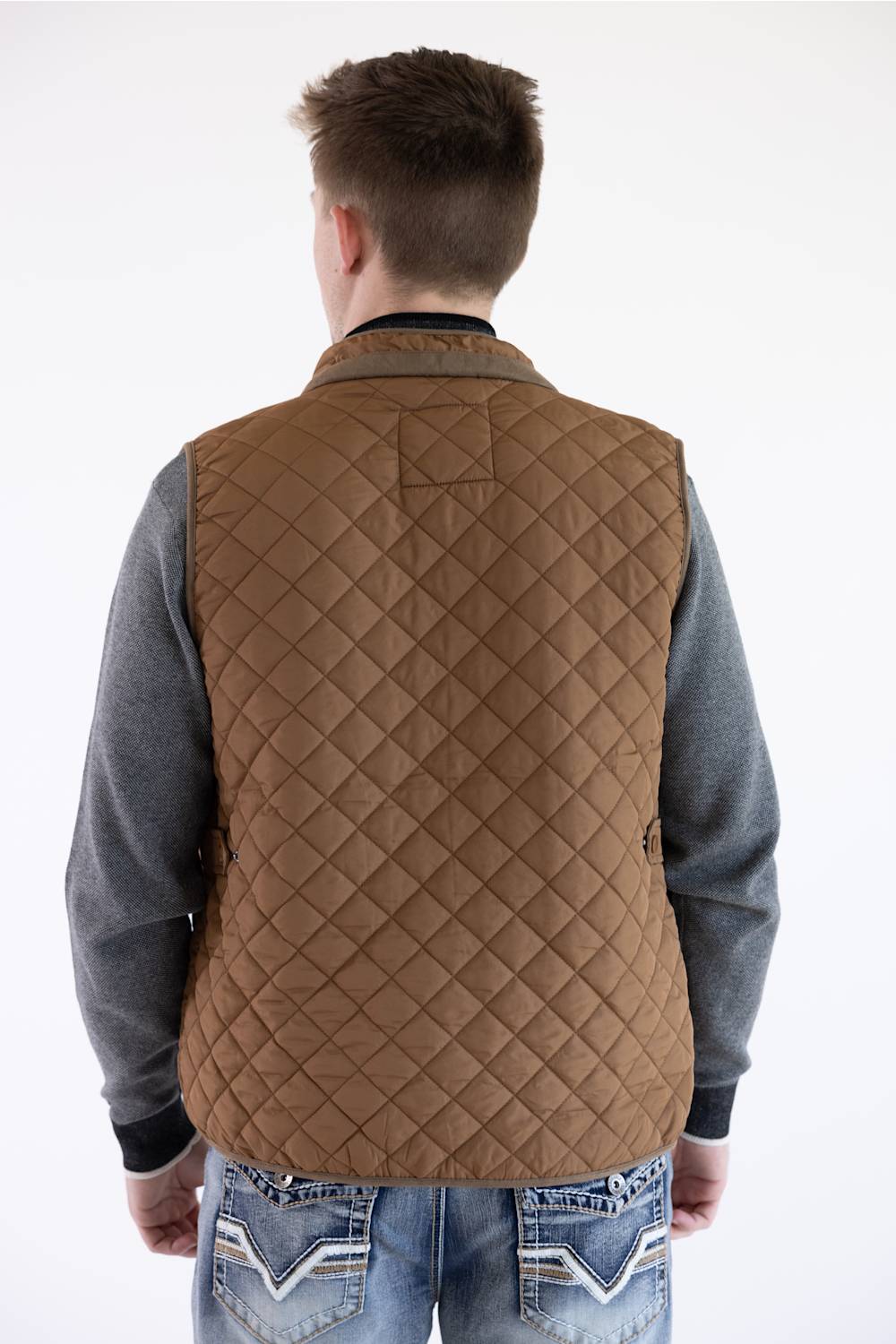 Back view of a model wearing a brown rhombus quilted vest, gray sleeves, and patterned jeans.