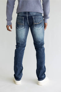 Rear view of a person wearing blue denim jeans with a light gray ribbed sweater and white sneakers against a plain light gray studio background.