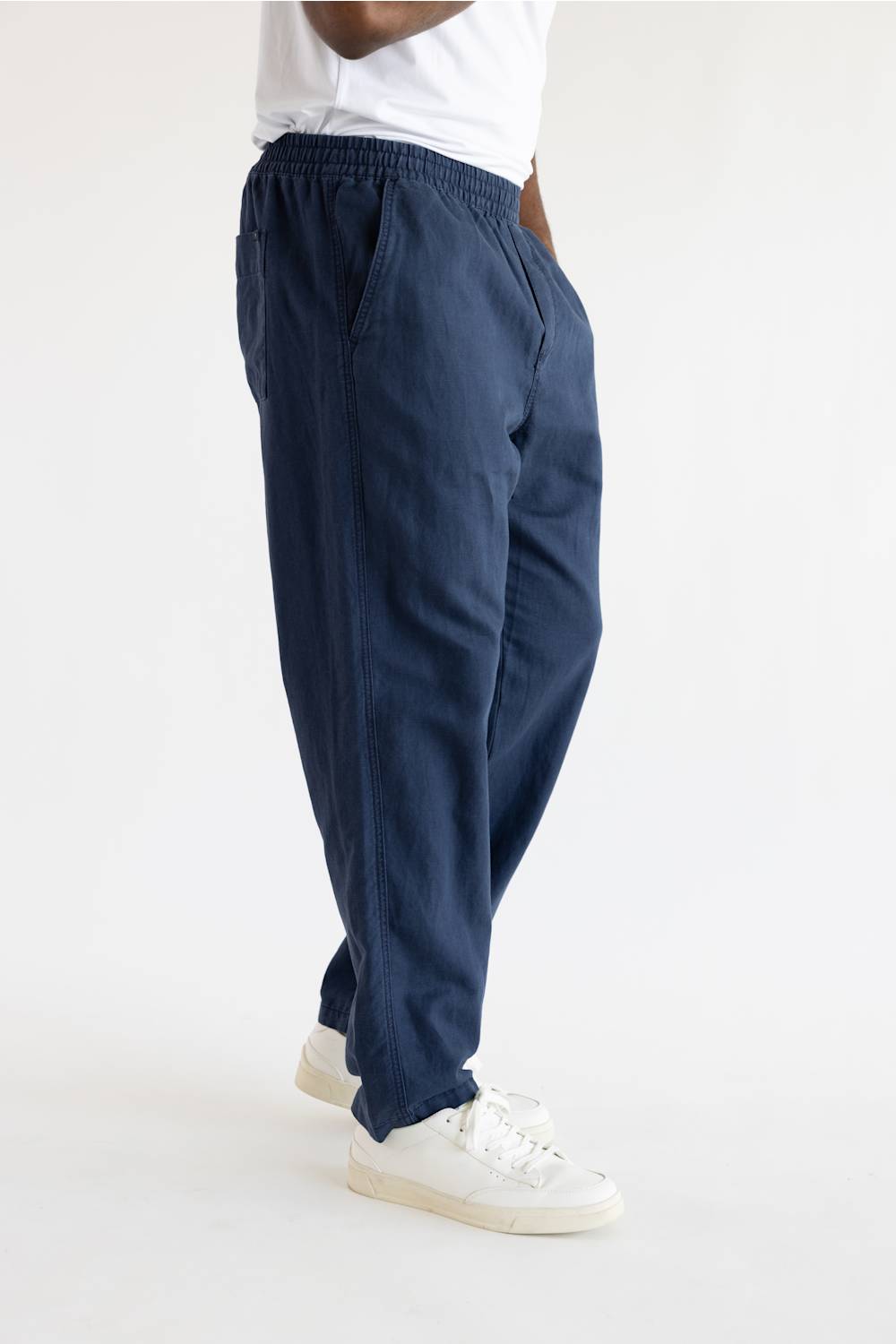 A person wearing loose navy blue drawstring pants with white sneakers, shown from the waist down against a plain white studio background.