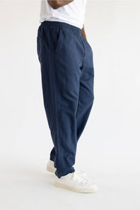 A person wearing loose navy blue drawstring pants with white sneakers, shown from the waist down against a plain white studio background.