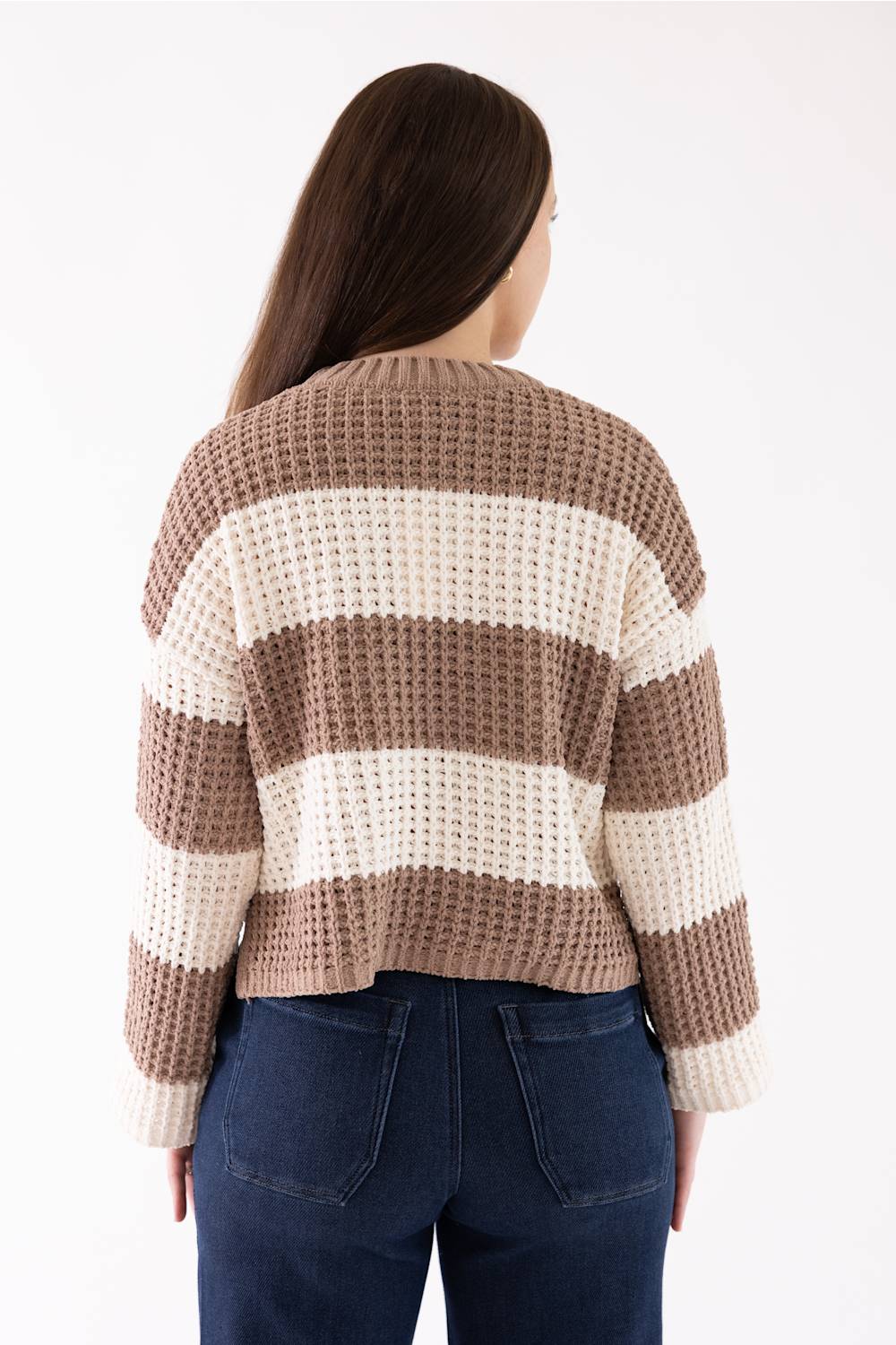 A woman viewed from the back wearing a waffle-knit cropped cardigan with horizontal brown and cream stripes, paired with dark blue jeans, against a plain white background.