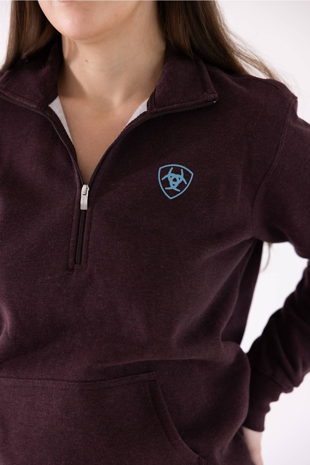 A close-up of a person wearing a dark plum quarter-zip fleece pullover sweatshirt with a small light blue shield logo on the left chest.