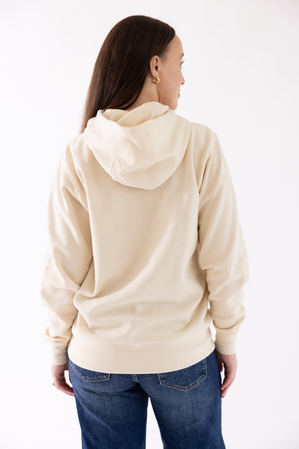 Back view showing the relaxed fit and hood of the parchment beige Ariat Wish You Were Here Hoodie, paired with dark blue denim jeans.