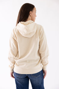 Back view showing the relaxed fit and hood of the parchment beige Ariat Wish You Were Here Hoodie, paired with dark blue denim jeans.