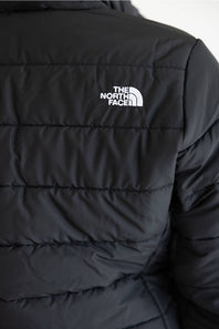 Close-up of a black puffer jacket showing horizontal quilting and the white embroidered The North Face logo on the upper chest.