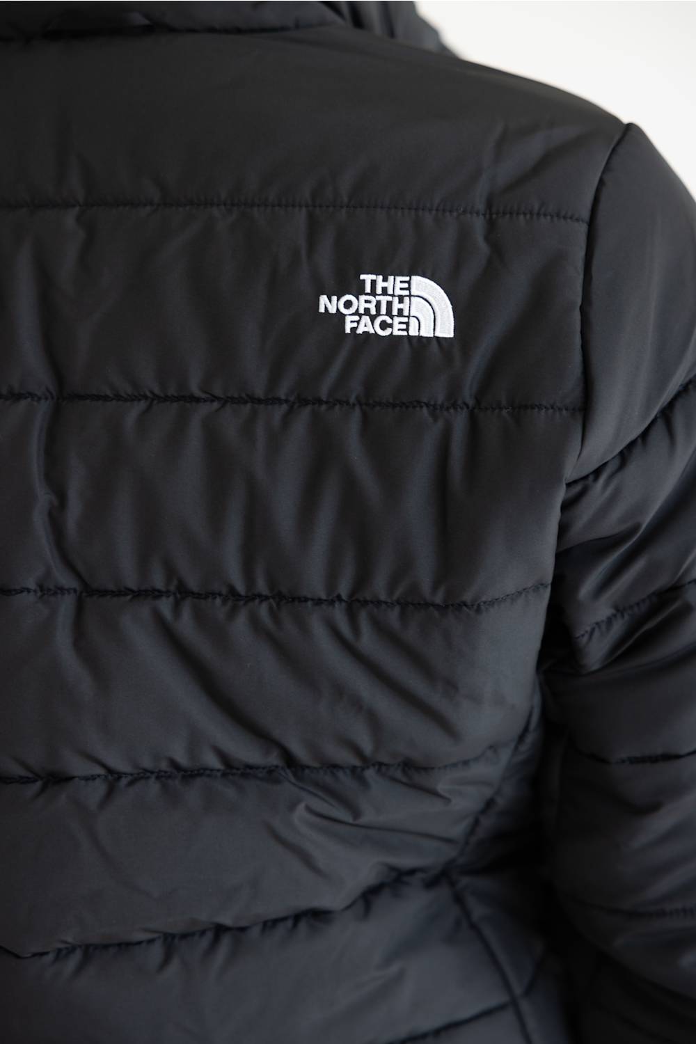Close-up of a black puffer jacket showing horizontal quilting and the white embroidered The North Face logo on the upper chest.