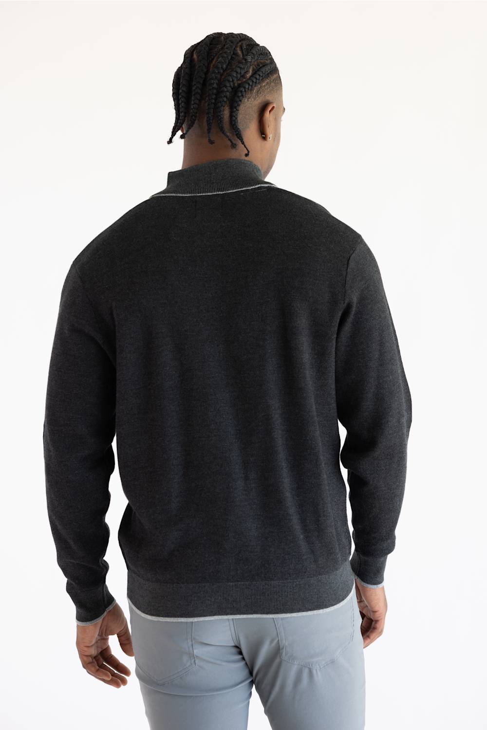 A man viewed from behind wearing a dark charcoal gray knit quarter-zip sweater with a contrasting light gray collar trim, paired with light gray trousers, against a plain white studio background.