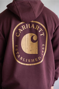 A close-up of a maroon hoodie showing the back, featuring a large distressed tan graphic with the text 'Carhartt Established 1881' and the brand's signature 'C' logo.