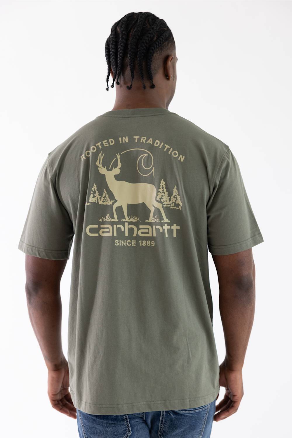 A man viewed from behind wearing a sage green Carhartt t-shirt with a large beige graphic on the back featuring a deer, trees, and the Carhartt logo.