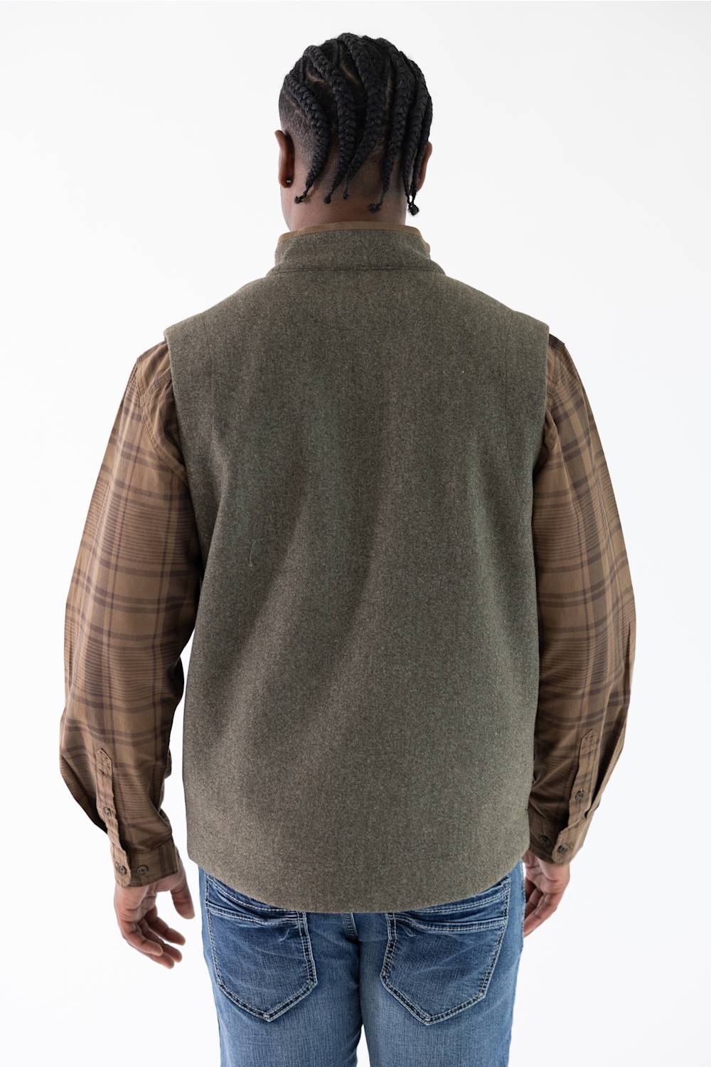 A man viewed from behind wearing an olive green vest over a brown and tan plaid flannel shirt, paired with blue jeans, against a plain white background.