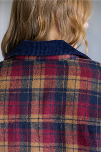 Close-up back view of a person wearing a plaid flannel-style jacket with a dark navy ribbed corduroy collar. The plaid pattern features red, navy, tan, and dark blue stripes.