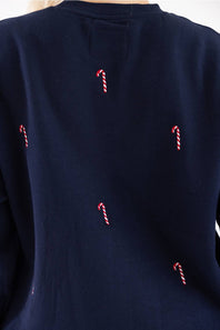 Close-up back view of a navy blue fleece crewneck sweatshirt featuring an all-over embroidered red and white candy cane pattern.