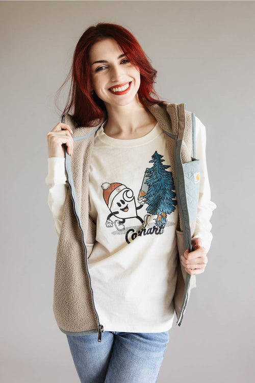 A smiling woman with red hair models a beige fleece zip-up hoodie over a cream graphic t-shirt featuring a cartoon character and the word 'Comfort', paired with blue jeans, against a plain light gray background.