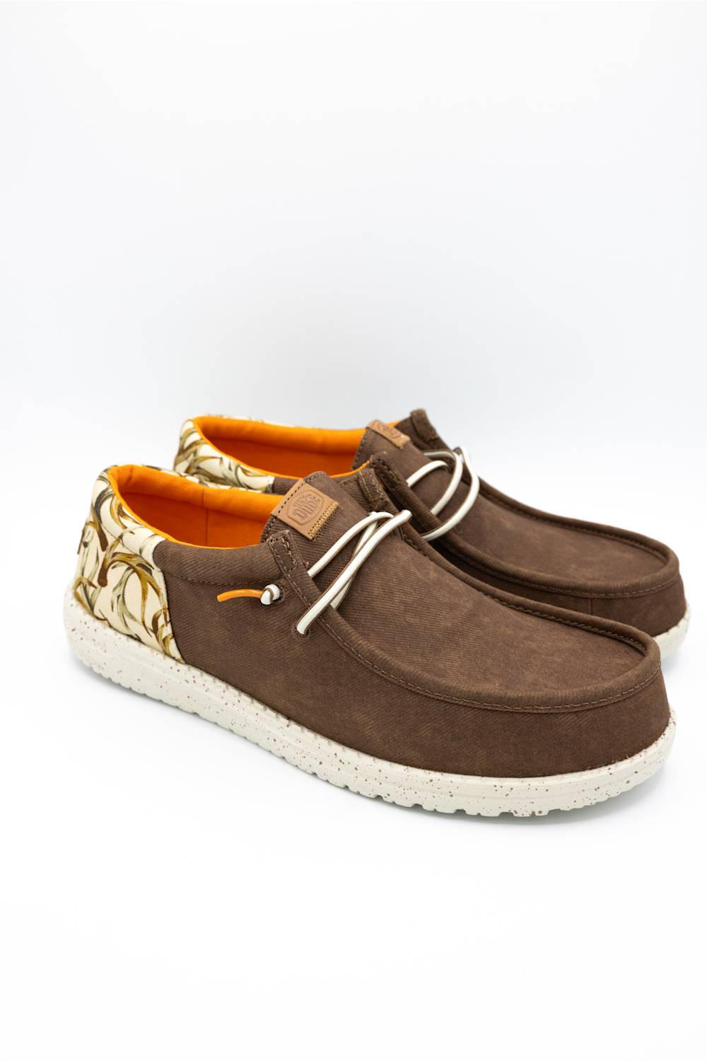 A pair of brown suede boat-style shoes with white laces, a patterned heel tab, and bright orange lining, shown on a clean white background.