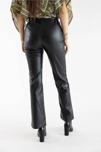 Rear view of a model wearing black faux-leather flare pants with a matching black belt, paired with a patterned top and black heels, against a white studio background.