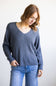 A woman wearing a slate blue ribbed knit sweater and blue jeans, standing against a plain white background.