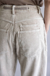 Close-up of the back waist and pockets of light beige corduroy trousers, showing the textured fabric, belt loops, and stitching.