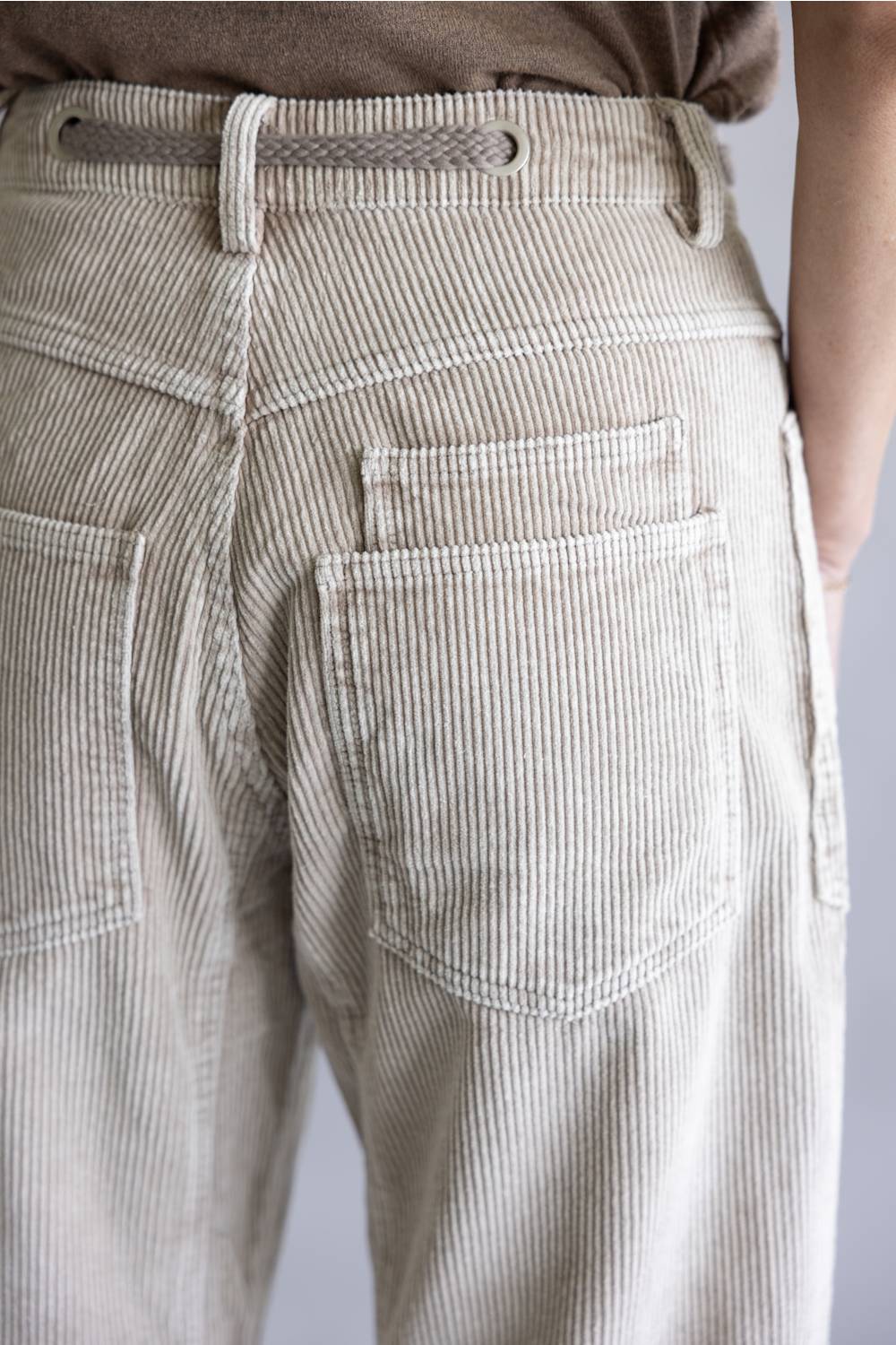 Close-up of the back waist and pockets of light beige corduroy trousers, showing the textured fabric, belt loops, and stitching.