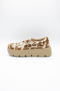 A single platform sneaker with a brown and cream cow-print pattern on the upper and a chunky beige sole, shown against a plain white background.