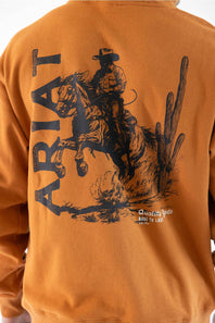 Close-up of the back of a burnt orange sweatshirt featuring a large black graphic print of a cowboy riding a bucking horse, with the word 'ARIAT' and desert illustrations.