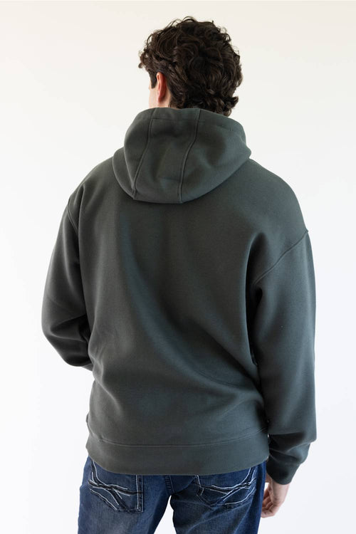 A man viewed from behind wearing a dark green pullover hoodie and blue jeans against a plain white background.