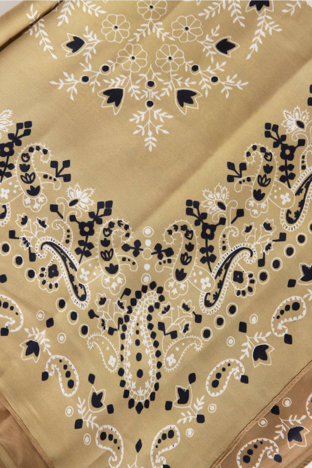 A close-up of a beige fabric with detailed black and white embroidery, featuring paisley and floral motifs.