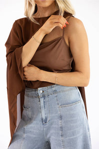 A woman wearing a brown sleeveless camisole top with sheer mesh panels and a draped brown shawl, paired with light blue jeans, against a plain white background.