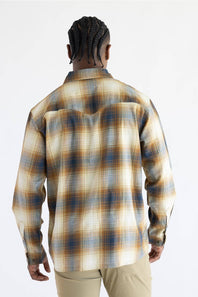 A man viewed from the back wearing a Carhartt long-sleeve plaid button-up shirt in beige, brown, and blue tones, paired with khaki pants, against a plain white background.