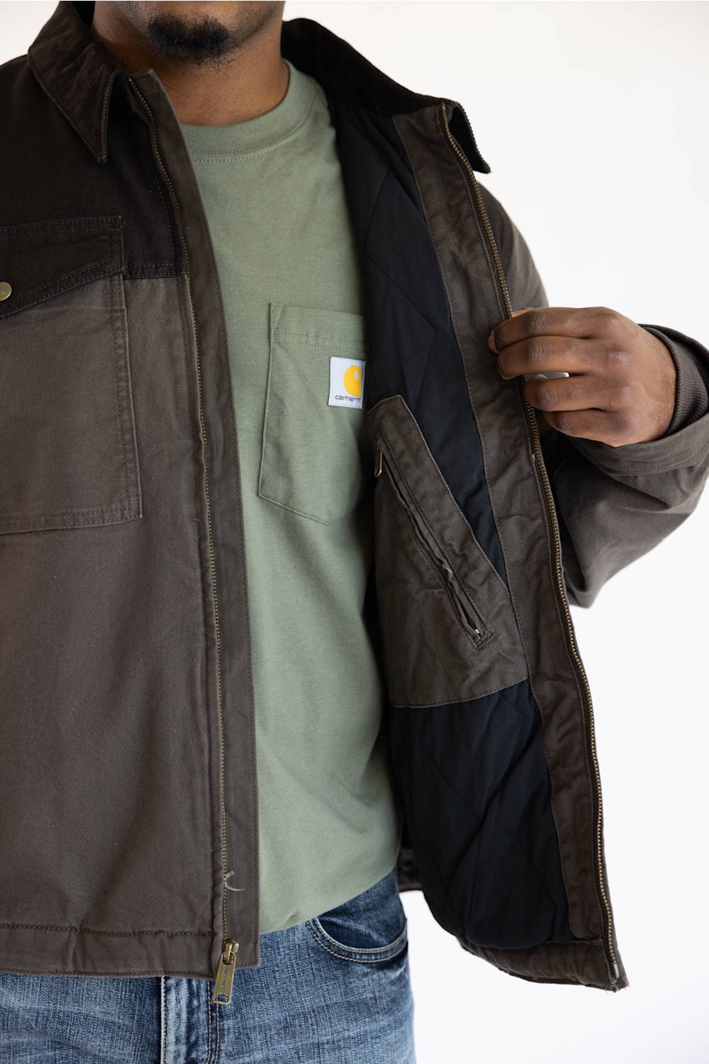 A person in a green t-shirt and jeans opens a brown jacket against a plain white background.