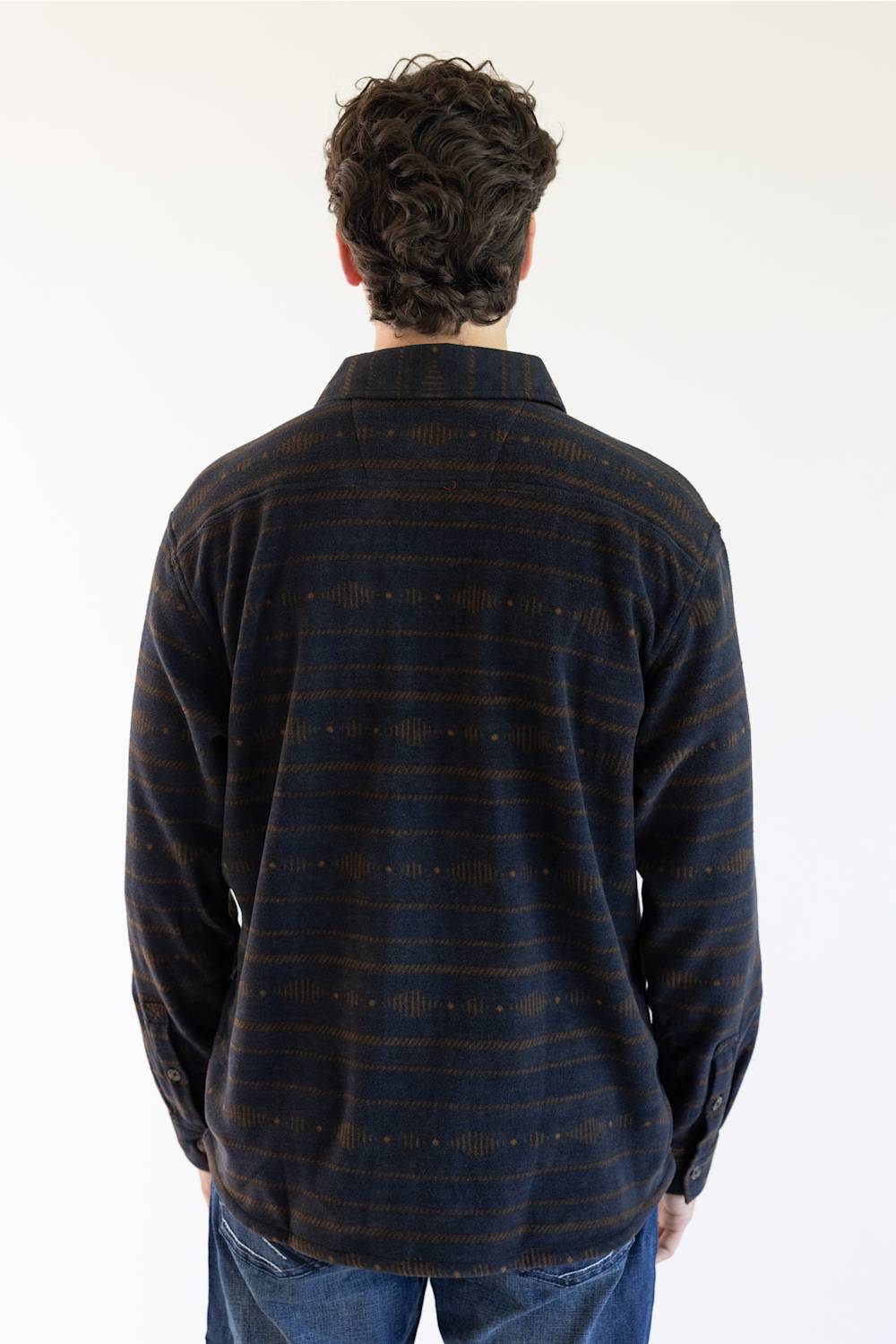 A man viewed from behind wearing a long-sleeve Carhartt plaid button-up shirt in navy and brown with thin orange stripes, paired with blue jeans, against a plain white background.