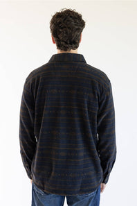 A man viewed from behind wearing a long-sleeve Carhartt plaid button-up shirt in navy and brown with thin orange stripes, paired with blue jeans, against a plain white background.