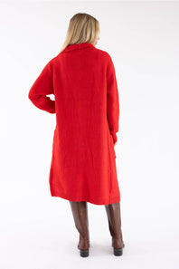A woman viewed from the back wearing a bright red knit cardigan or long sweater coat with brown knee-high boots, against a plain white studio background.