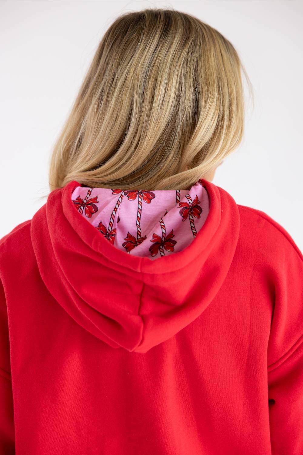 A person viewed from the back wearing a bright red hoodie with a pink inner hood lining featuring a red and black floral pattern, against a plain light gray background.