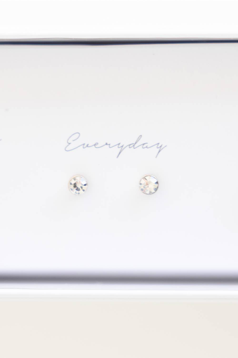 A pair of small round stud earrings with clear faceted gemstones on a white display card that reads 'Everyday'.
