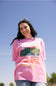A woman wearing a pink Billabong graphic t-shirt with a green turtle and orange starfish, photographed outdoors against a clear blue sky.