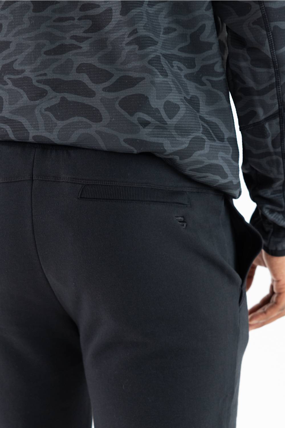 Close-up of a person wearing dark black patterned athletic pants and a matching dark long-sleeve top, focusing on the back waistband and pocket area.