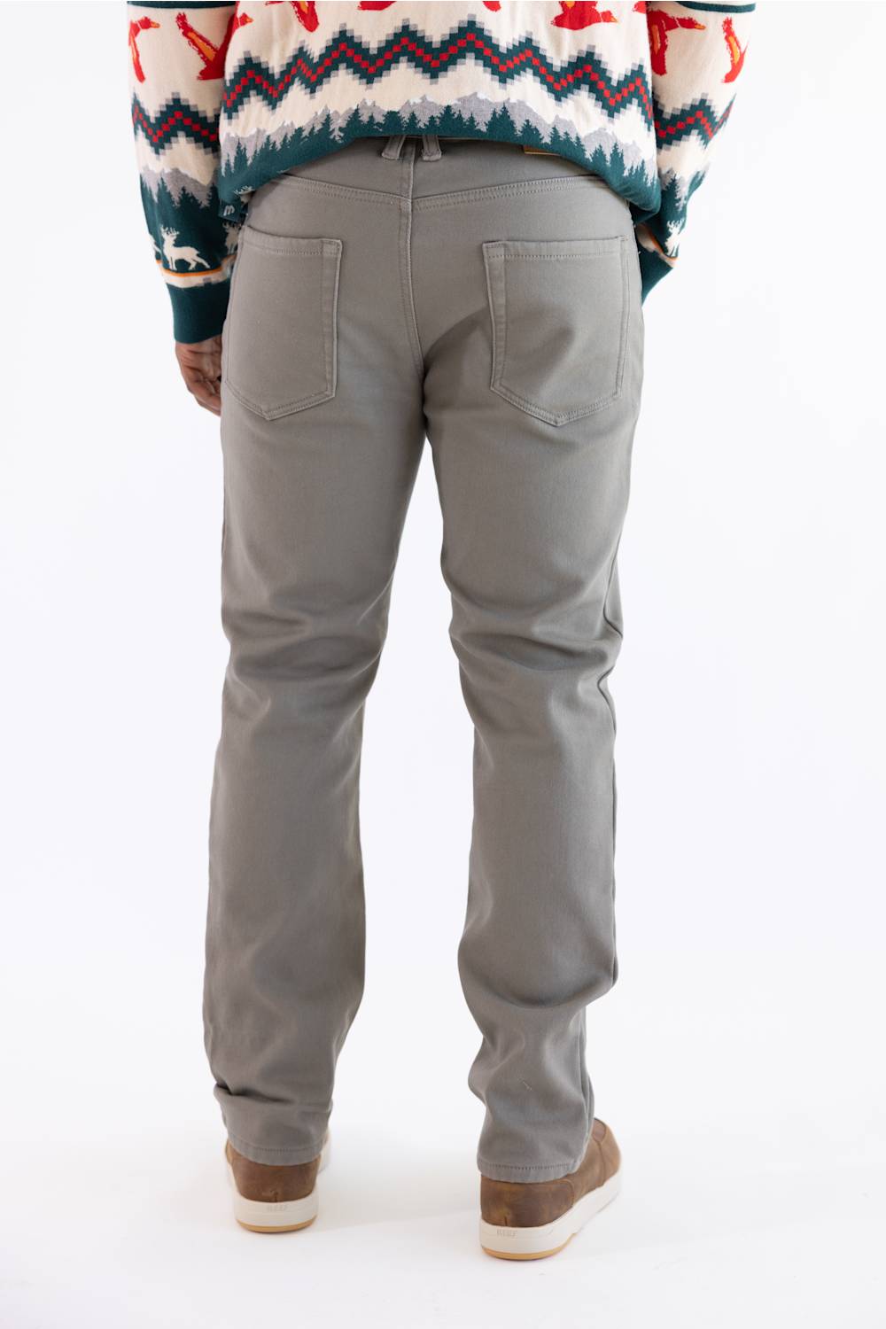 A person shown from the back wearing light gray slim-fit jeans, a multicolor patterned sweater, and brown shoes against a plain white background.