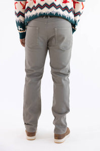A person shown from the back wearing light gray slim-fit jeans, a multicolor patterned sweater, and brown shoes against a plain white background.